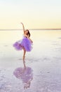 Girl ballerina in a ballet dress dances in the water of the lake at sunset.