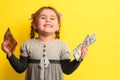 Girl with banknotes in hands on a yellow background, business child with world currency.