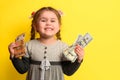 Girl with banknotes in hands on a yellow background, business child with world currency.