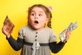 Girl with banknotes in hands on a yellow background, business child with world currency.