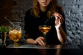 Girl at bar holds small sword with cherries over glass with cocktail