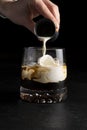 A girl bartender prepares a White Russian cocktail and pours cream into it.