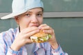 Girl in a baseball cap eats a hamburger with meat, front view, close-up Royalty Free Stock Photo