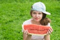 A girl in a baseball cap holds a large slice of watermelon in her hands in front of her Royalty Free Stock Photo