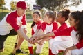 Girl baseball team kneeling with their coach, touching hands