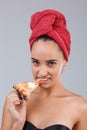 A girl, with bath towel on her head, appetizingly bites a slice of pizza. On a gray background.