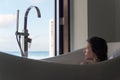 Young woman in bathtub admiring the view from the window. Tropical holiday destination