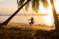 The girl on the beach rides on a swing during sunset. Sunset in the tropics, enjoying nature. Swing tied to a palm tree by the Royalty Free Stock Photo