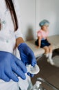 Girl beautician in a medical glove holds a cotton pad and a used bottle. Blue background. Medical and cosmetic content Royalty Free Stock Photo