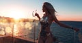 Girl in a beautiful bathing suit at sunset by the sea holding sunglasses