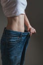 Young woman dressed in wide jeans and a white shirt, demonstrates successful weight loss. concept of diet and weight loss Royalty Free Stock Photo