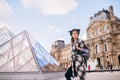 A girl in a beautiful coat stands near the Louvre