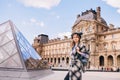 A girl in a beautiful coat stands near the Louvre