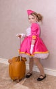 A girl in a beautiful fashionable dress with a child's suitcase.