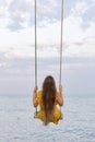 Girl with beautiful long hair sits on swing on sea background. Back view. Vertical frame Royalty Free Stock Photo