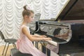 girl in a beautiful pink dress playing on a black grand piano. Girl playing on a black piano. Royalty Free Stock Photo