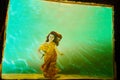 Girl in a beautiful yellow dress under water behind of glass. Female model posing under water in swimming pool Royalty Free Stock Photo