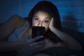 Girl in bed using mobile phone late at night at dark bedroom lying happy and relaxed