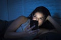 Girl in bed using mobile phone late at night at dark bedroom lying happy and relaxed Royalty Free Stock Photo