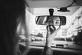 The girl behind the wheel looks in the rear-view mirror in the car and makes herself a make-up in black and white Royalty Free Stock Photo
