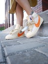 A girl in a beige dress and cream sneakers Nike poses on the background