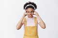 Girl believes she can move object with power of mind. Portrait of funny and angry cute female in dungarees, headband and