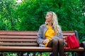 The girl on the bench is waiting for the guy. A beautiful young lady in a yellow dress is resting in the park.