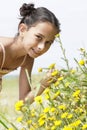 Girl Bending Down To Smell Flower In Field