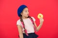 Girl in beret hat hold donut red background. Kid playful girl eat donut. Health and nutrition concept. Sweet life