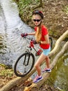 Girl on bicycle fording throught water on log .