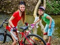 Girl on bicycle fording throught water onto log in park.