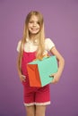 Girl with big smile holding colorful paper bag. Model with orange and green gift box. Child with long blond hair wearing Royalty Free Stock Photo