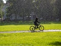 Girl bikes in urban park with rain and sunshine
