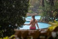 A girl in a bikini sits on the side of an outdoor pool in a tropical garden in the rain Royalty Free Stock Photo