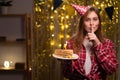 Girl in a birthday hat holding a cake and covering her mouth with a finger having a secret Celebrating birthday at home Royalty Free Stock Photo