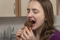 Girl is biting chocolate cake. Young woman tastes eclair with chocolate icing Royalty Free Stock Photo