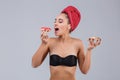 A girl in a black bra and with a red towel on her head tries to bite a donut and in other hand holds a piece of pizza.