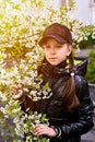 Girl in a black cap and jacket among white cherry blossoms. Artistically colored and tinted photography