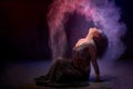 Girl in black dress posing in dark studo during photoshoot with flour or dust and light. Dangerous witch during struggle between