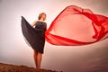 A girl in black dress with red fabric dances on sand dunes against a dramatic sky before a thunderstorm. Model posing