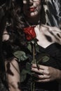 A girl in a black dress with red lips and a red rose. Black shadow patterns on the face.