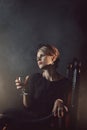 A girl in a black dress is sitting on a chair with a glass of wine Royalty Free Stock Photo