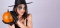 A girl in black gloves holds a pumpkin. Funny woman in a witch hat and makeup for Halloween Royalty Free Stock Photo