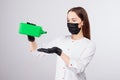 Girl in black gloves and mask pours liquid from green jar, disinfectant solution, light gray background, woman with long hair in