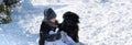 Girl with black Golden-doodle lying on snow in winter day. Concept of dog friendship Royalty Free Stock Photo