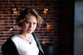 The girl in a black jacket and a light blouse poses opposite to a window, a background the brick wall covered with glow lamps. Royalty Free Stock Photo