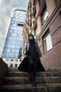 Girl in black leather coat and hood with laptop on city street, concept of woman hacker and agent working remotely at computer Royalty Free Stock Photo