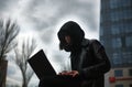 Girl in black leather coat and hood with laptop on city street, concept of woman hacker and agent working remotely at computer Royalty Free Stock Photo