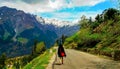 A girl in a black long coat and a red crossbody bag walking along the path to the Himalayan mountains. Royalty Free Stock Photo