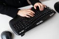 A girl in a black outfit typing on a full-sized black keyboard with a mouse. The keyboard has various function keys and